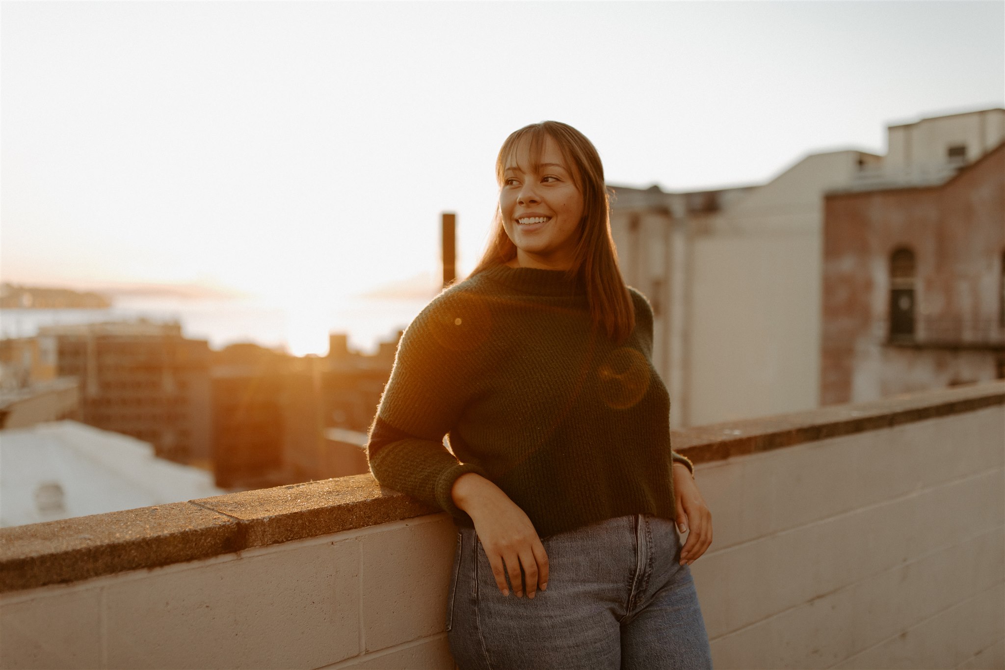 W woman stands on a rooftop in the city as the sun sets behind her.