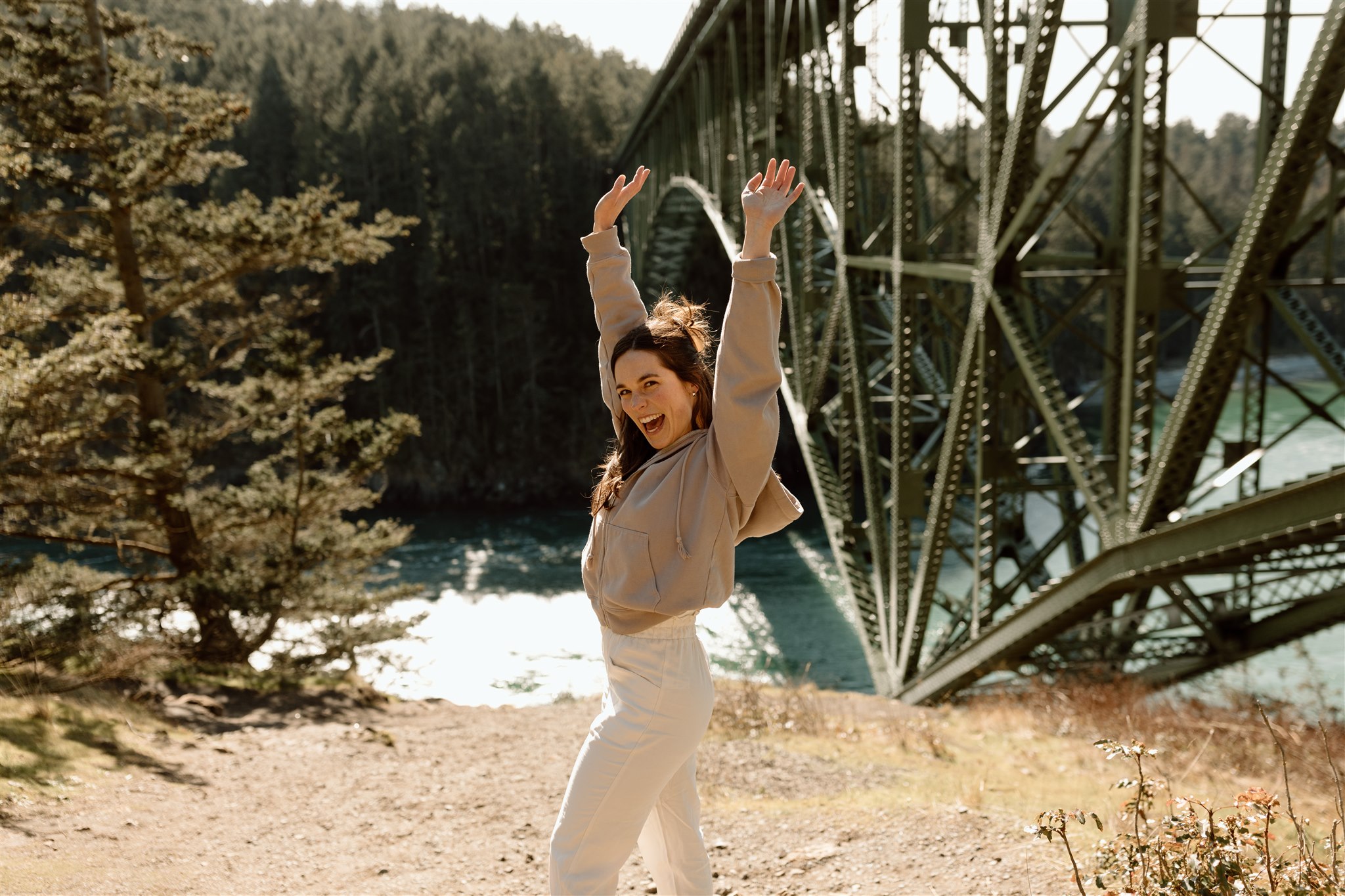 A woman raises her hands in excitement near a bridge.