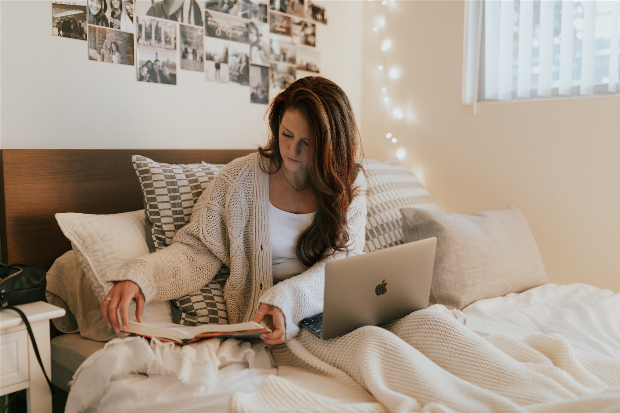 A young woman reads her Bible and studies her laptop from her bed.