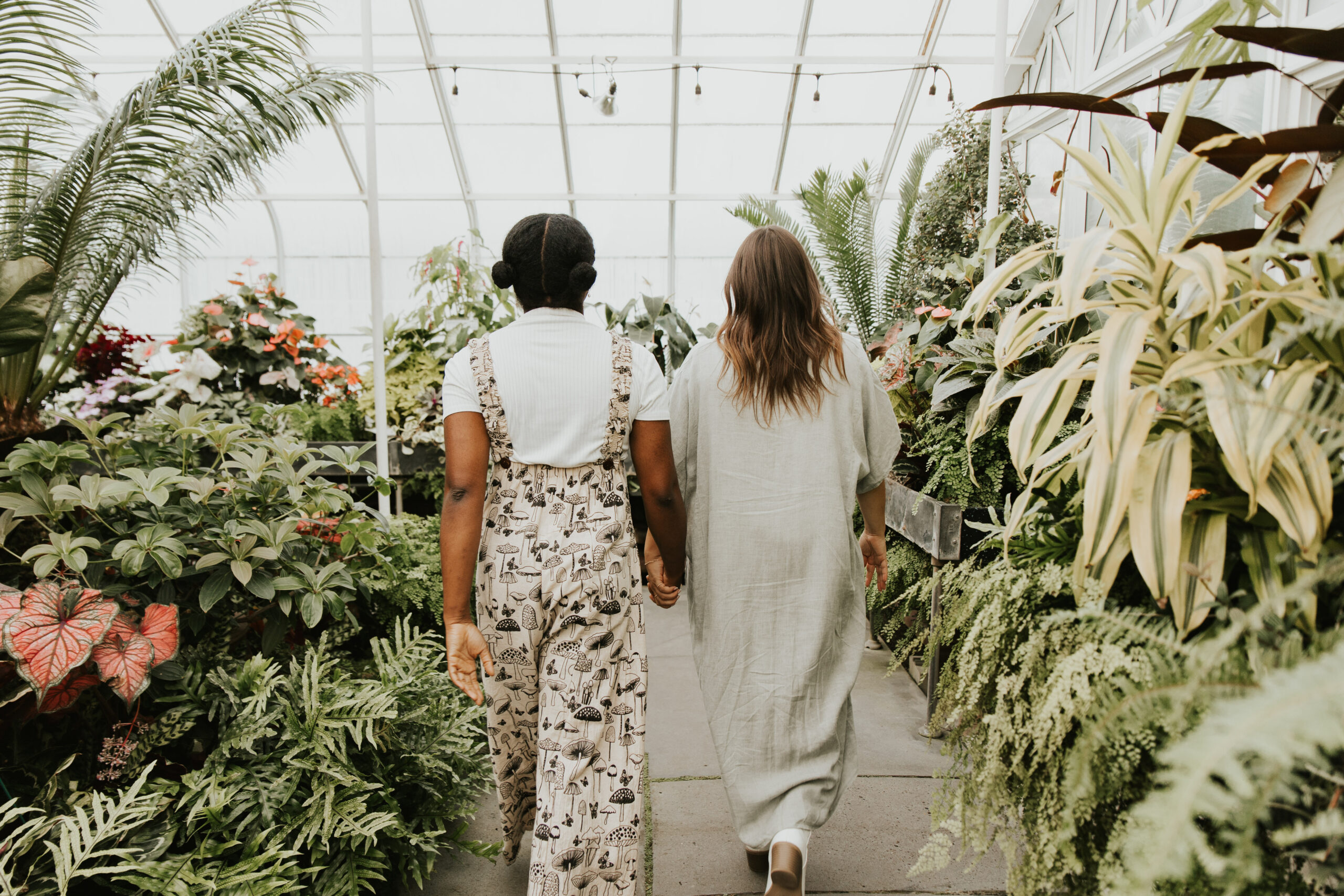 Two women walk hand-in-hand through a peaceful garden.